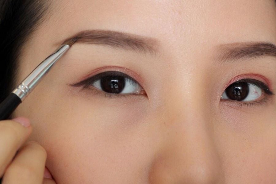 Một người đang sử dụng cọ trang điểm để vẽ chân mày trên khuôn mặt.