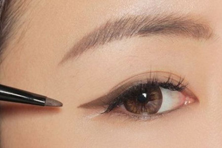 Cận cảnh mắt với bút kẻ mắt đang vẽ đường viền, nhấn mạnh hàng mi và lông mày gọn gàng.