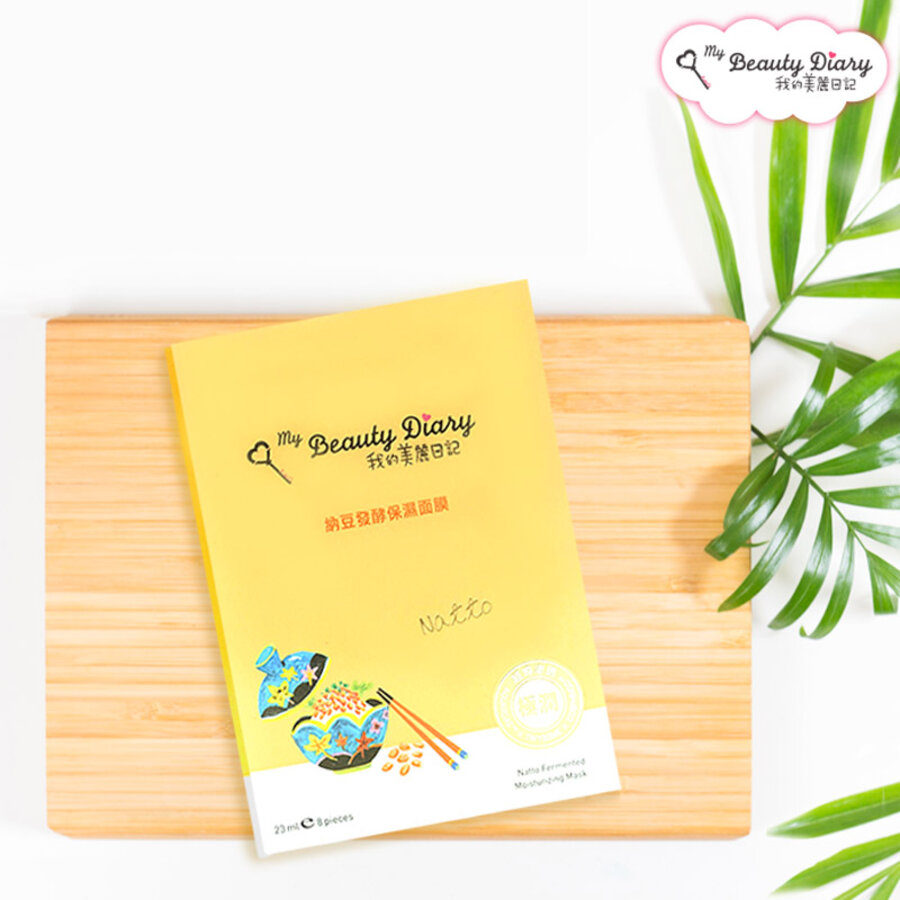 Mặt nạ dưỡng da trong bao bì màu vàng đặt trên khay gỗ, bên cạnh có một nhánh lá xanh.