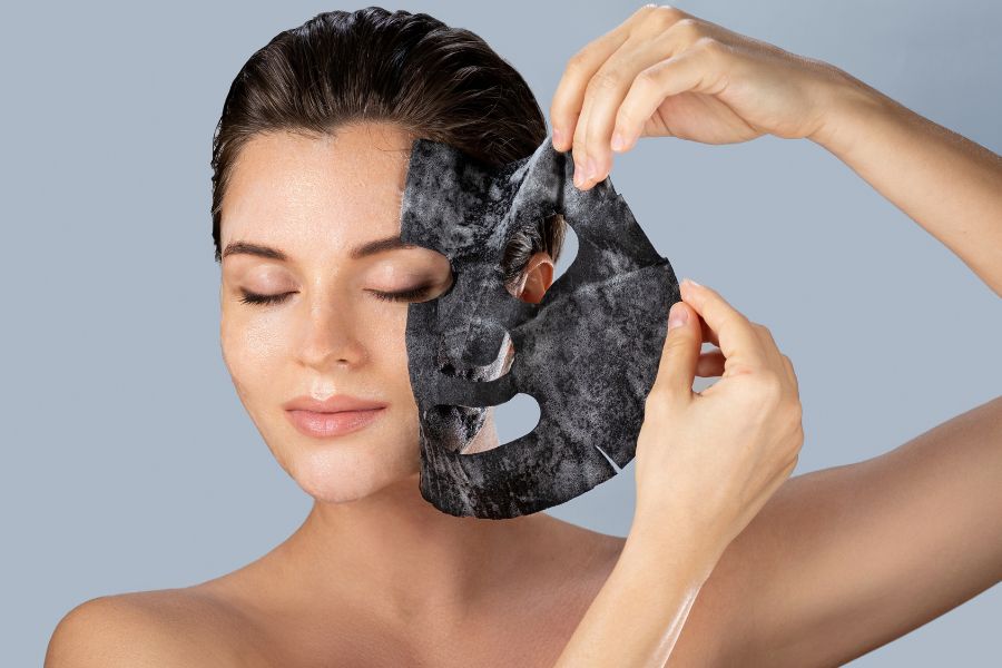 Người đang tháo mặt nạ dưỡng da màu đen, mắt nhắm, trên nền xám.