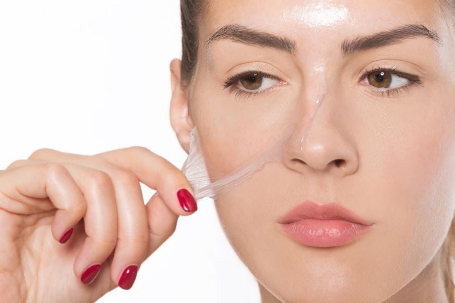 Người phụ nữ đang bóc lớp mặt nạ trong suốt trên mặt, tay sơn móng màu đỏ.
