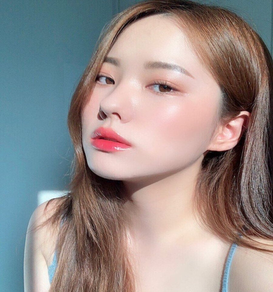 Người phụ nữ tóc dài, trang điểm nhẹ, ánh sáng chiếu sáng khuôn mặt, nền xanh nhạt.