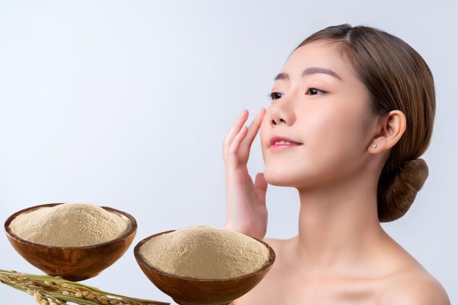 Người phụ nữ chạm vào mặt với hai bát bột thiên nhiên phía trước, trên nền trắng.