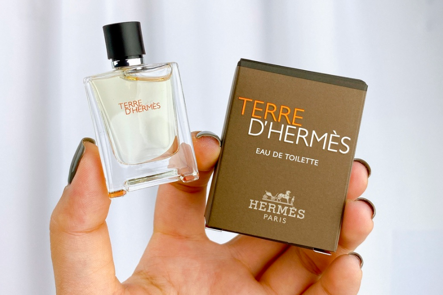 Người cầm chai nước hoa Terre D'Hermès và hộp màu nâu với chữ trắng và cam.