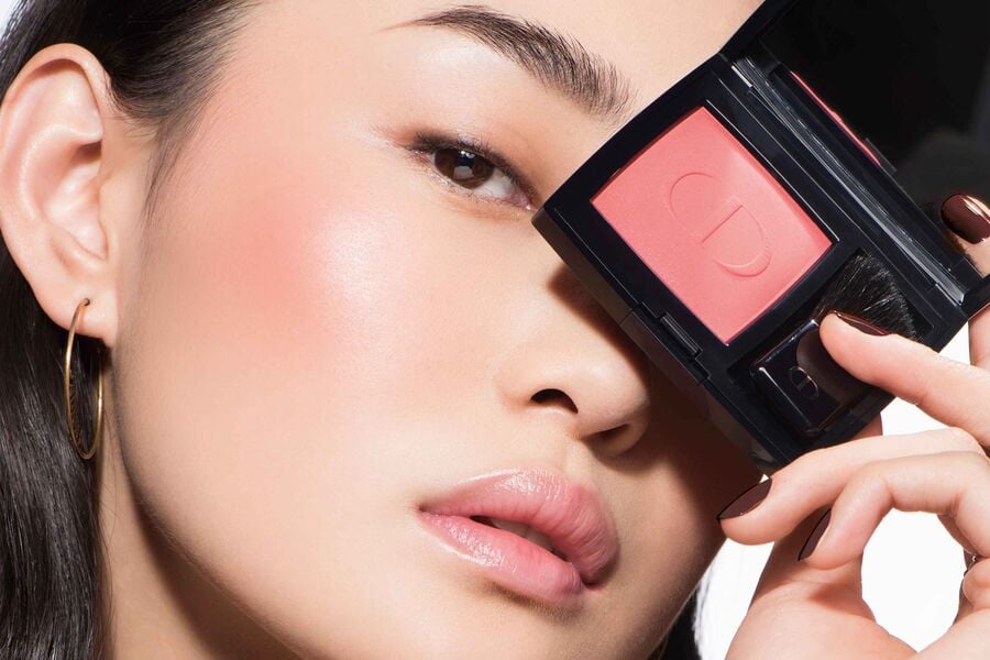 Người mẫu cầm hộp phấn má hồng màu cam, che một phần khuôn mặt, tạo ánh nhìn tinh tế.