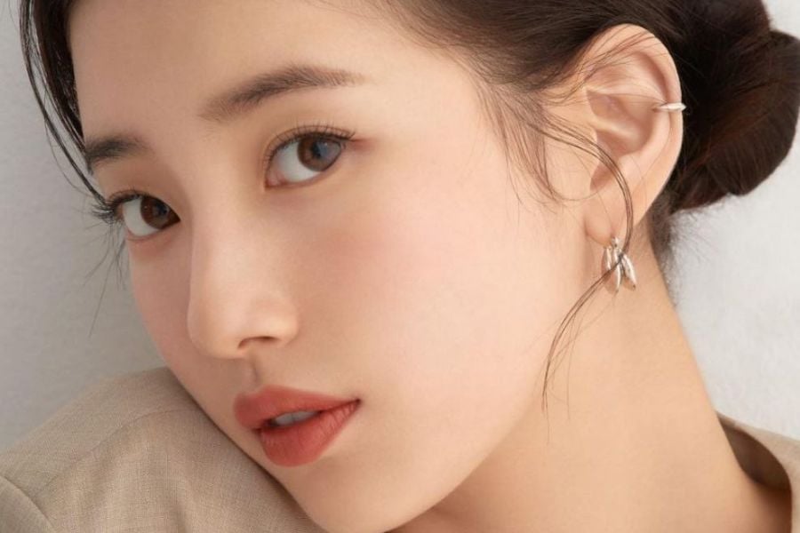 Cận cảnh khuôn mặt của một người với mái tóc búi và trang điểm tinh tế, đeo hoa tai bạc.