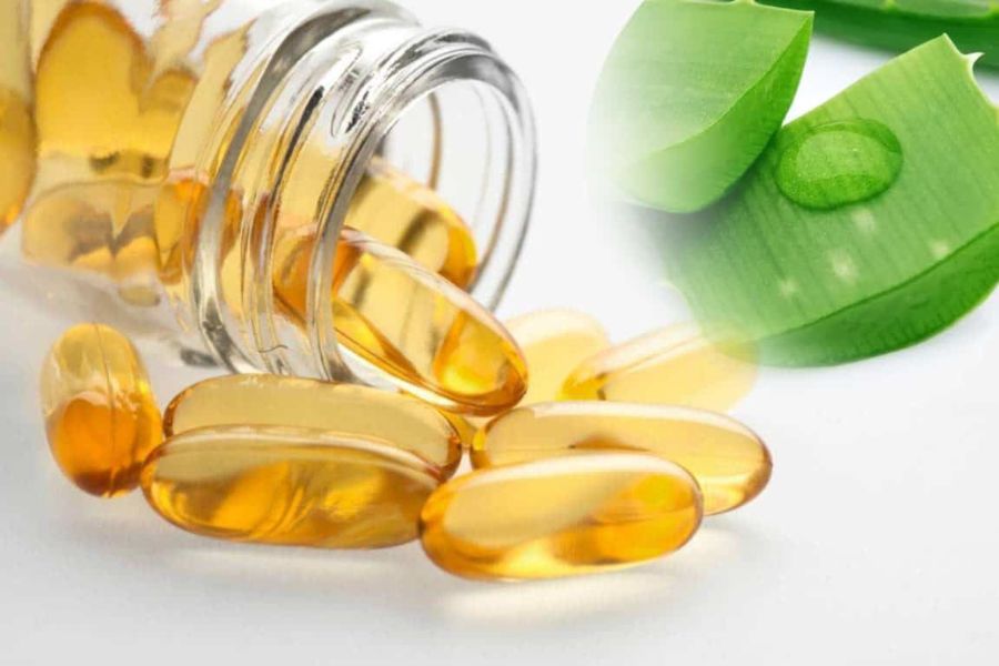Viên nang màu vàng từ chai thủy tinh đổ ra, cạnh lá cây xanh với giọt nước trên bề mặt.