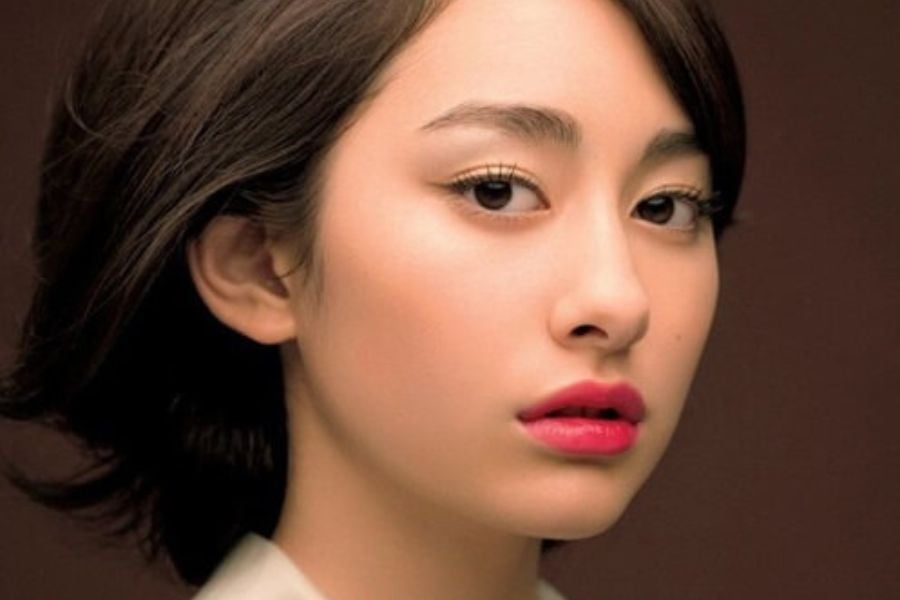 Người phụ nữ với mái tóc ngắn và trang điểm nhẹ nhàng, nền màu nâu.