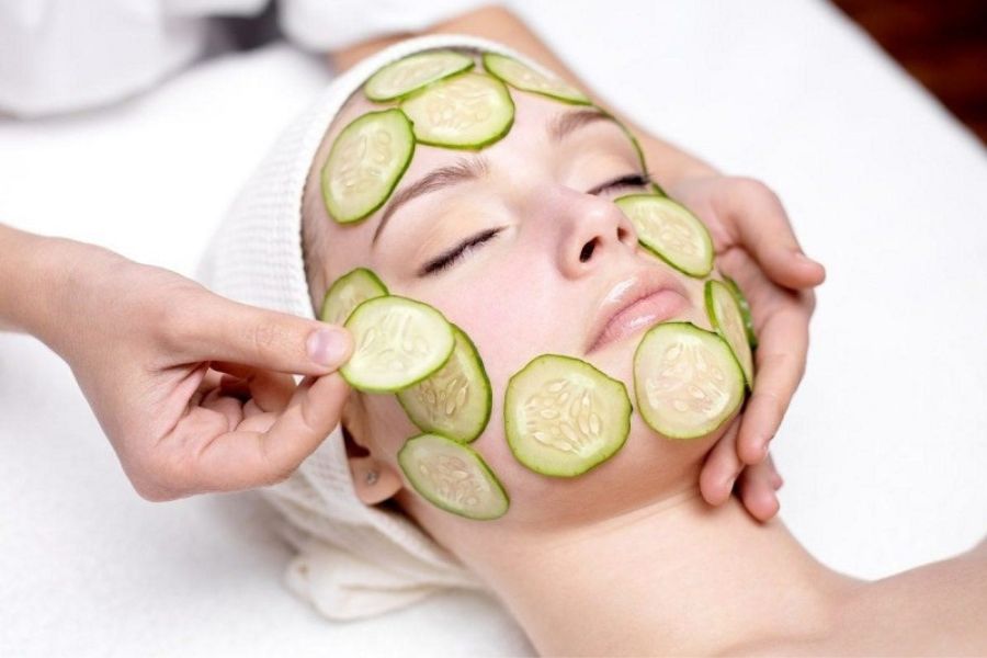 Người đang thư giãn với các lát dưa leo đặt trên mặt, được chăm sóc bởi một đôi tay.