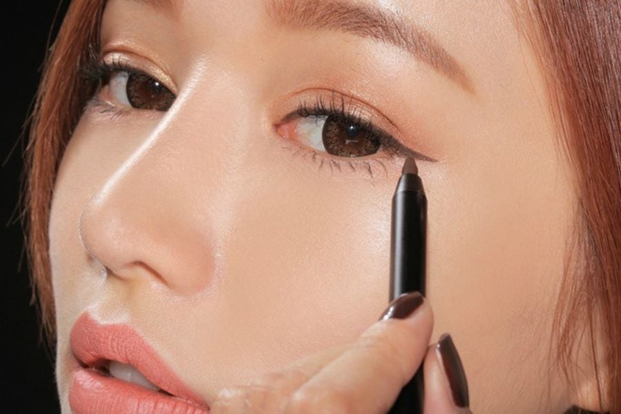Người đang sử dụng bút kẻ mắt để trang điểm, tập trung vào vùng mắt với màu sắc tự nhiên.