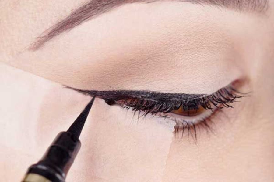 Một người đang kẻ mắt bằng bút kẻ mắt màu đen, tạo đường nét dọc theo mi mắt trên.