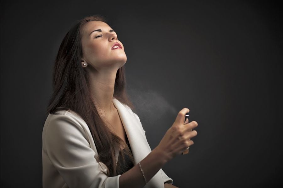 Người phụ nữ nhắm mắt và xịt nước hoa lên cổ, nền tối.