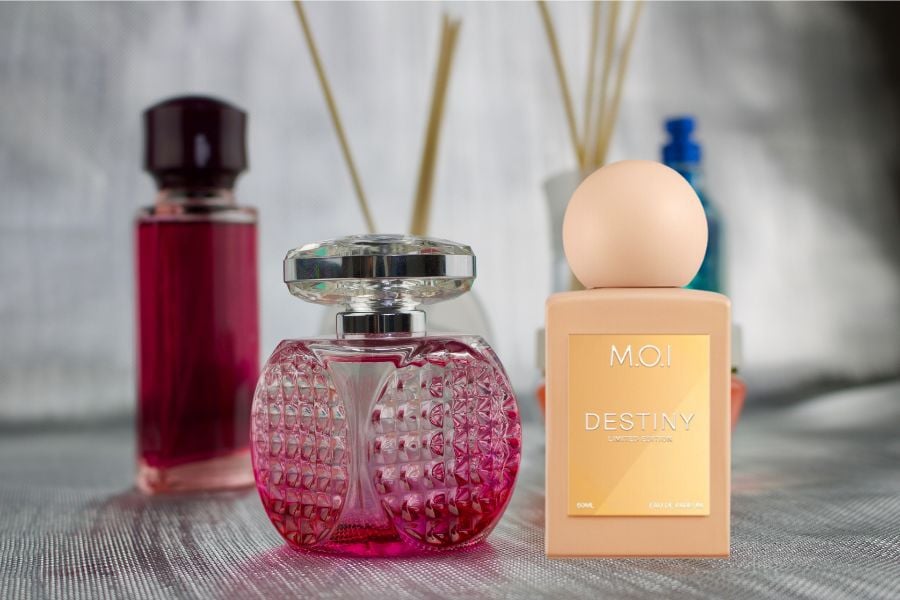 Các chai nước hoa nhiều màu sắc được đặt trên bề mặt vải, nền mờ với que khuếch tán phía sau.